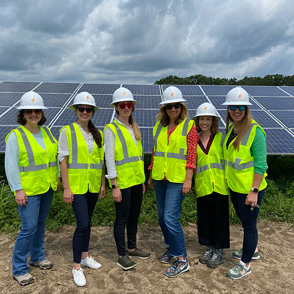 Six women of Catalyze team in a solar field wearing safety vests