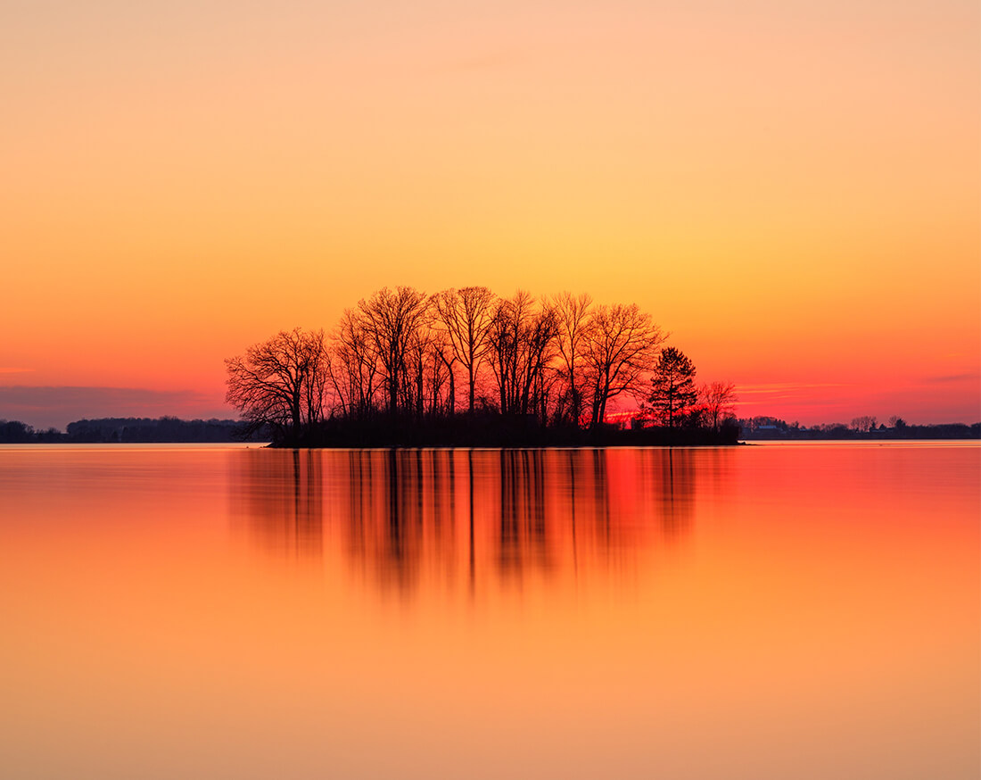 Orange and red sunset photo of a small island on a quiet lake