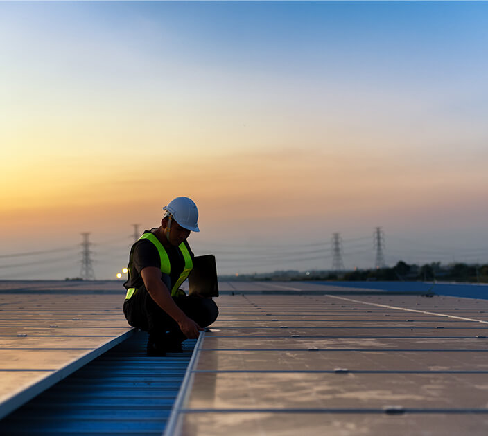 A renewable energy technician on a roof surveying solar panels